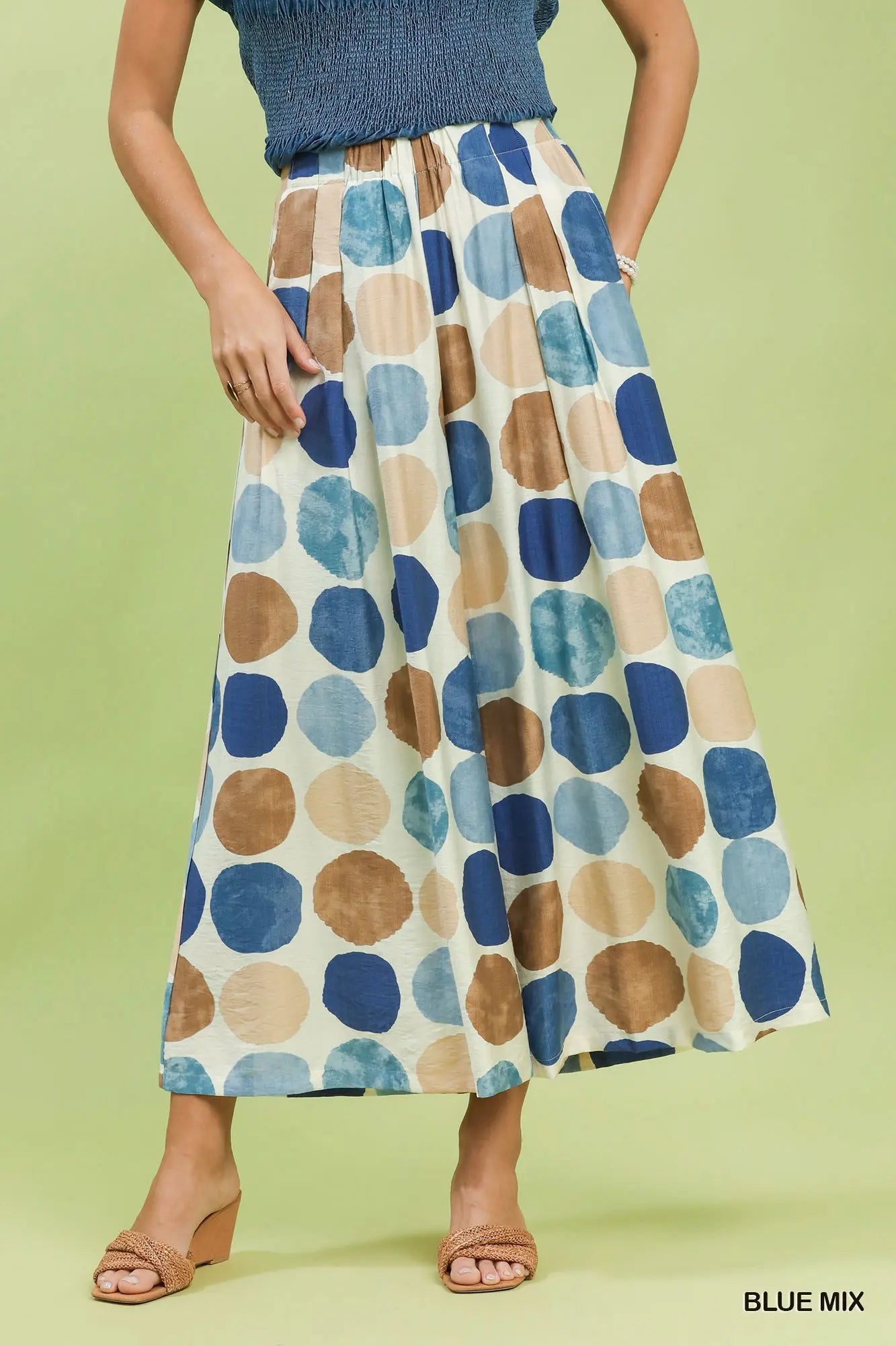 Person wearing a patterned wide leg pant with blue and brown polka dots on a green background