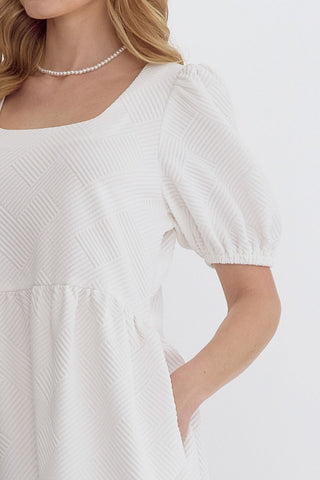 Entro white textured dress with a pearl necklace on a light background closeup