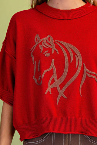 A close-up of a Grigio bright red knit sweater featuring a large light brown  horse head design on the front, worn by a model.
