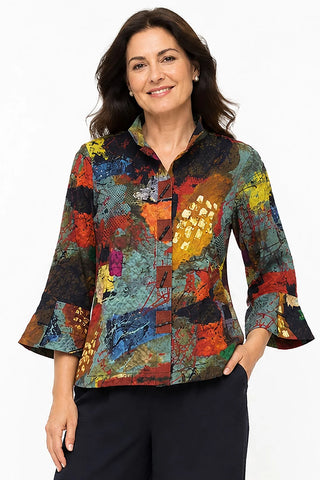 A woman modeling an Ali Miles long-sleeve button-up blouse with a vibrant, multicolored abstract patchwork print, paired with dark slacks.