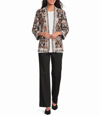 A woman models an Ali Miles three-quarter sleeve open-front jacket featuring a beige, brown, and black floral pattern with a black-and-cream zigzag trim, styled with black wide-leg pants and black heels.