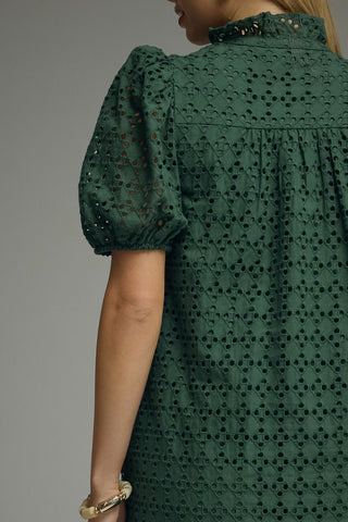 A close-up back view of a woman wearing a dark green eyelet lace dress with puff sleeves and a high neckline.