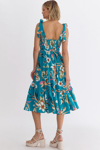 Woman wearing an Entro turquoise blue floral dress with a back view showing a smocked back