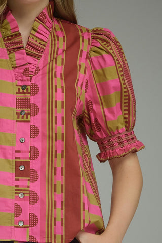 A close-up of a woman wearing a short-sleeve blouse with a bold vertical striped pattern in pink, olive green, and brown, featuring puff sleeves and a ruffled collar.