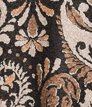 A close-up of a textured fabric featuring a dark charcoal black background with a distressed, cracked-look damask design in beige, cream, and warm tan.