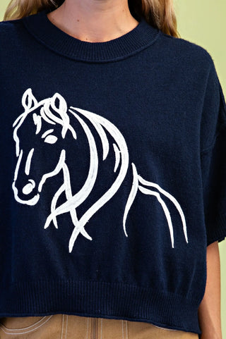 A close-up of a navy blue knit sweater featuring a large white line-art graphic of a horse on the front, worn by a model.