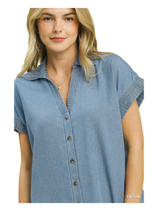 A woman wearing a light blue denim short-sleeve button-up shirt with textured trim on the collar and sleeve cuffs, shown against a plain white background.