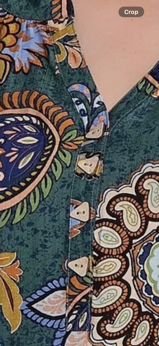 Close-up of a patterned garment with a V-neckline, featuring a dark green base with intricate paisley and floral motifs in blue, orange, beige, and yellow. 