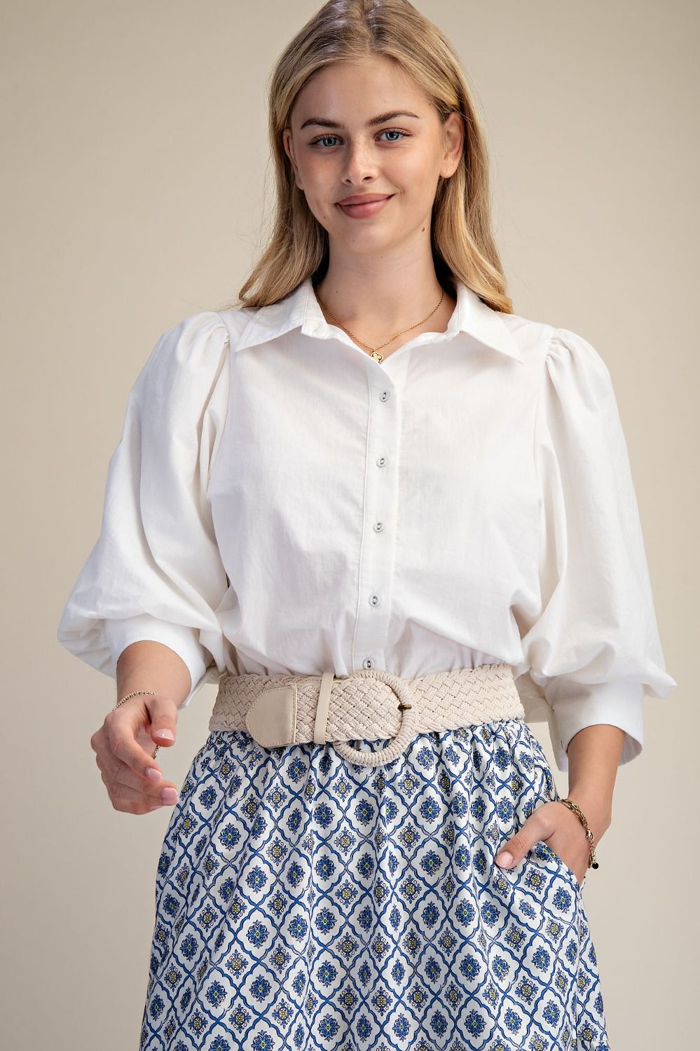 Woman wearing a white blouse and patterned skirt against a beige background