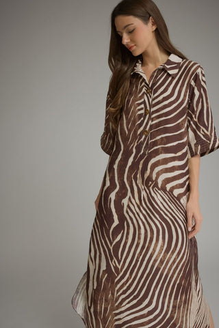 A woman wearing a brown and beige zebra-print midi shirt dress, standing against a neutral gray studio background.