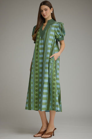 A woman modeling a green and light blue patterned midi dress with puff sleeves, a V-neckline, and side pockets.