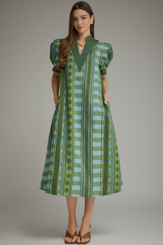 A woman modeling a green and light blue patterned midi dress with puff sleeves, a V-neckline, and side pockets.