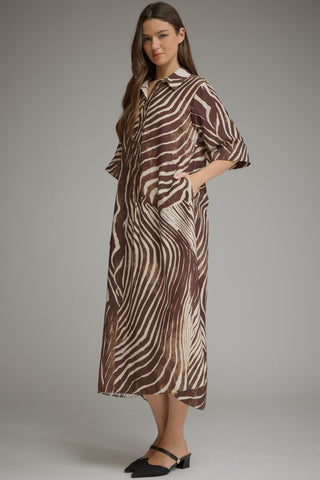 A woman modeling a brown and beige zebra-print midi shirt dress with three-quarter sleeves and a collar, paired with black flat shoes, against a neutral gray studio background.