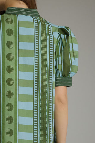 A close-up of a woman wearing a short-sleeve collared blouse with vertical stripes in olive green, light blue, and white, featuring puff sleeves and geometric patterns.