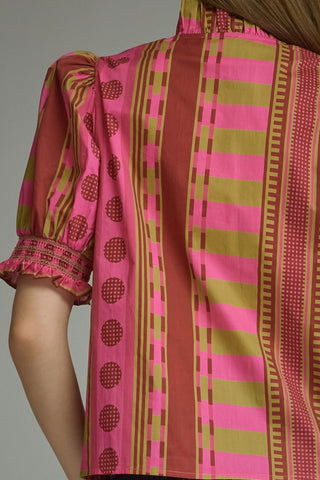 A close-up of a pink and olive green patterned blouse with puff sleeves and a smocked cuff, worn by a model.