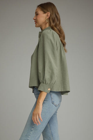 A woman shown in side profile wearing an Entro sage green cropped blouse with voluminous sleeves and light blue jeans, photographed against a plain gray studio background.