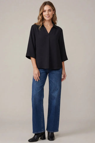 A woman modeling a She & Sky black three-quarter sleeve slip on blouse with blue wide-leg jeans and black boots.