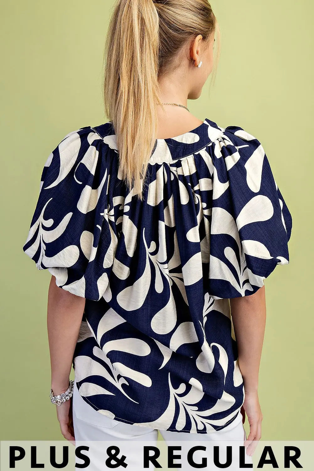 Woman wearing a navy and off white patterned blouse against a green background