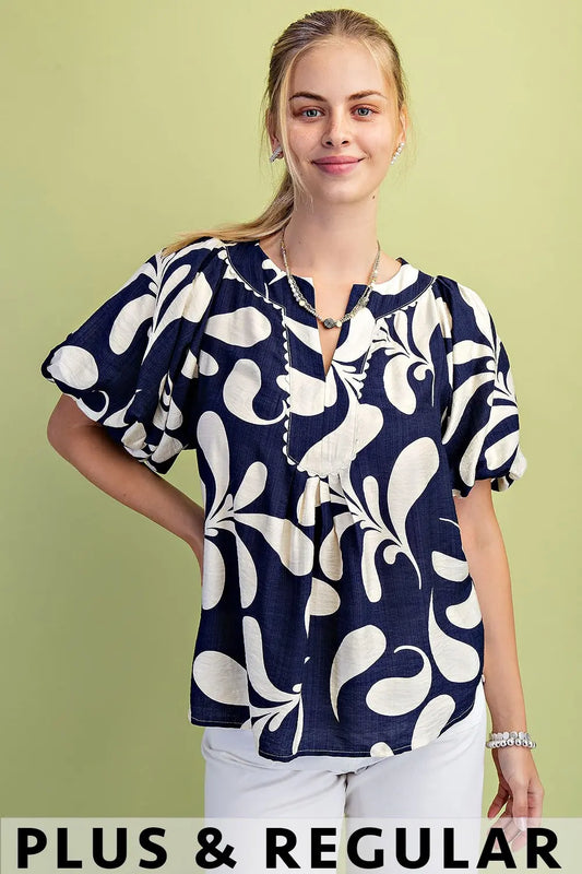 Woman wearing a Gigio navy and off white patterned vneck blouse against a green background