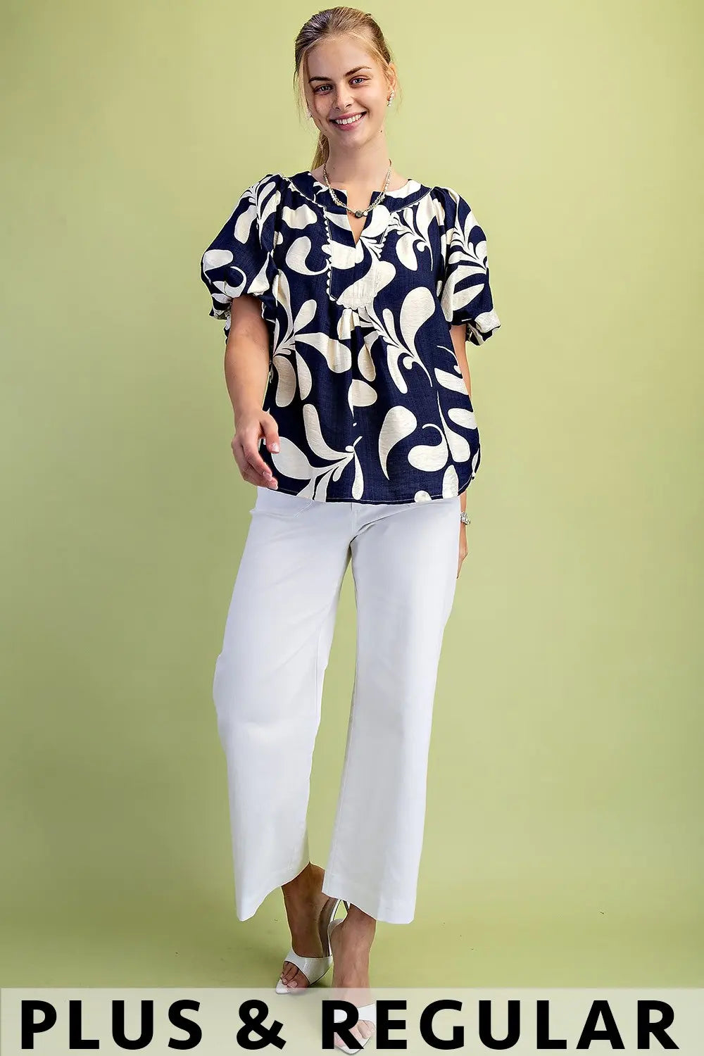 Woman wearing a patterned top and white pants on a green background
