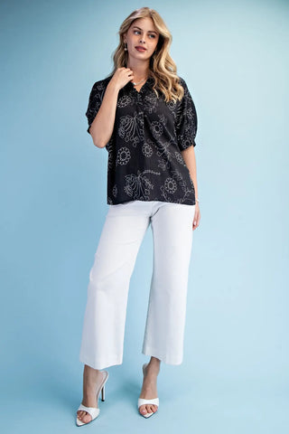 Woman wearing a black patterned blouse and white pants from Gigio top style #TE1999