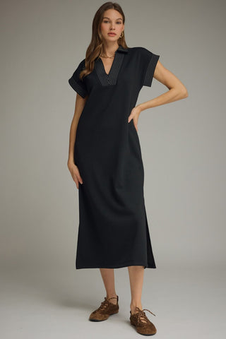 A woman models an Entro black midi dress with a V-neckline, short sleeves, and top stitching details on the chest and sleeve cuffs. 