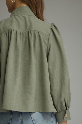 Close-up back view of a woman wearing an Entro olive green long-sleeve blouse with gathered shoulders and blue jeans against a plain gray studio background.