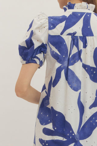 White dress with blue floral pattern worn by a person on a plain background