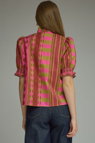A woman viewed from the back wearing a Entro short-sleeve blouse with vertical pink, olive green, and plum stripes, paired with dark blue jeans, against a solid gray studio background.