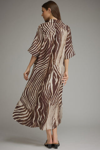 A woman modeling a brown and beige zebra-print kaftan dress, shown from the back against a neutral gray studio background.