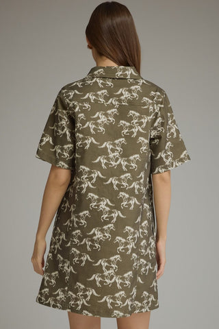 A woman viewed from the back wearing a Entro short-sleeve collared dress with an allover white horse print on an olive green base.