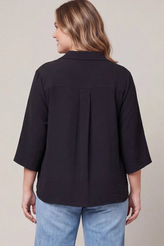 A plus size woman shown from the back wearing a She & Sky black three-quarter sleeve slip on shirt with a pleated back detail, paired with light blue jeans.
