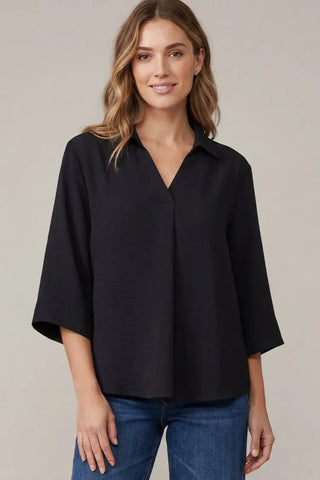 A woman wearing a She & Sky black three-quarter sleeve button-down blouse with a V-neck, paired with blue jeans.