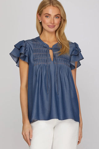 Woman wearing a blue denim She & Sky blouse with ruffled sleeves
