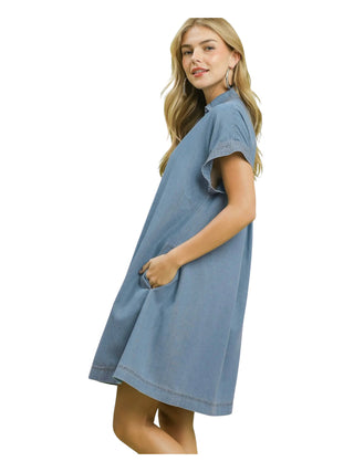 A woman modeling a light blue denim dress with short sleeves and a high collar, shown from a side-back angle against a plain white background.