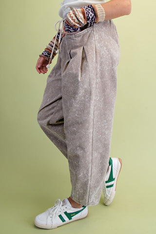 A person wearing Easel loose, faded taupe-brown twill pants with a drawstring waist, styled with a patterned knit sweater and white sneakers.