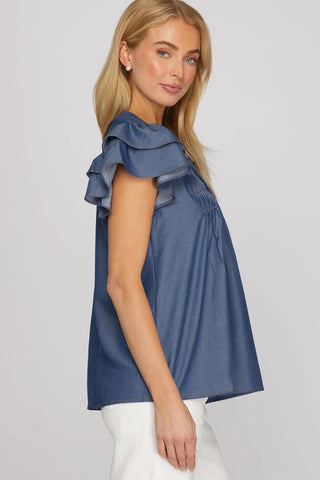 Woman wearing a She & Sky blue denim ruffled blouse against a plain background 