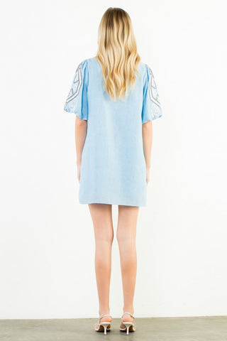 A woman viewed from behind wearing a THML light blue short-sleeve dress with embroidered sleeves.
