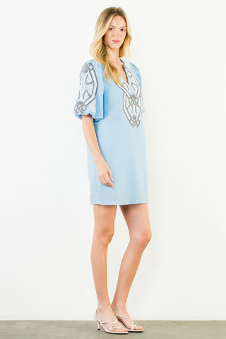 A woman modeling a light blue mini dress with silver embroidery on the chest and puff sleeves, paired with clear high-heeled sandals,
.