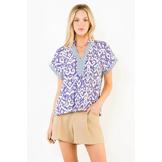 A THML short-sleeve V-neck blouse with a purple and white geometric pattern and light blue trim. Style #FTM3517