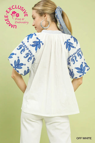 Woman wearing a white blouse with blue floral embroidery on a light green background